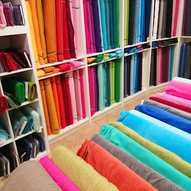 Bunte Stoffe in Regalen und auf einem Tisch, verschiedene Farben und Texturen.